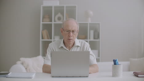 Un-Anciano-Está-Trabajando-Con-Una-Computadora-Portátil-En-Casa-Escribiendo-Mensajes-Y-Revisando-El-Correo-Electrónico-De-Forma-Remota,-Trabajo-Para-Jubilados